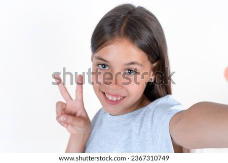 Positive young beautiful kid girl wearing grey T-shirt  take selfie make v-sign