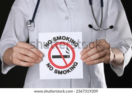 Doctor holding card with no smoking sign on black background, closeup