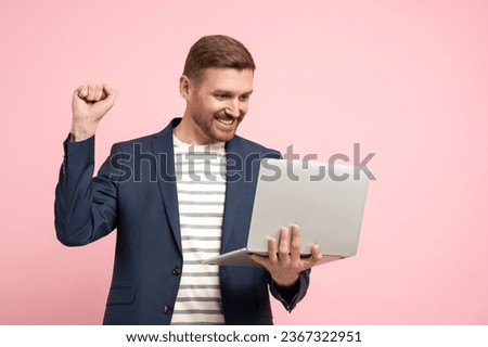 Positive man winner trader, crypto investor, entrepreneur, financier looking at laptop screen showing win yes gesture on pink background. Bearded attractive smiling guy on advertisement banner poster.