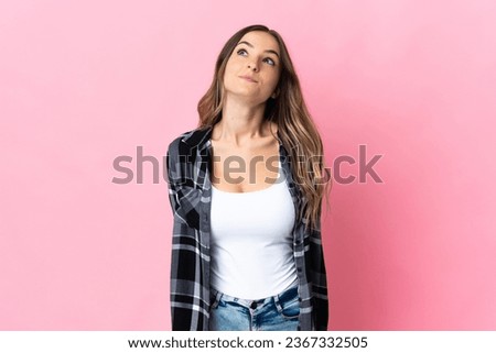 Young Romanian woman isolated on pink background and looking up