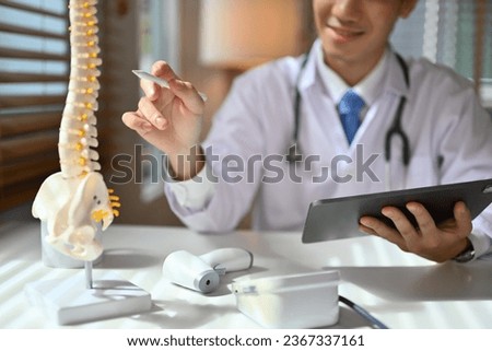 Orthopedists holding digital tablet and pointing at model. Concept of osteoporosis, back pain, lumbar, chiropractic and health. Royalty-Free Stock Photo #2367337161