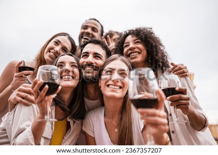 Bottom view of multiracial group of friends having drinks in a rooftop party. Diverse young happy group of millennials drinking wine in a terrace taking a picture.