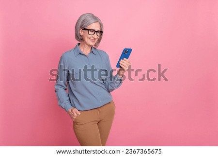Photo of lovely positive pensioner lady wear trendy clothes hold use iphone samsung stand empty space isolated on pink color background