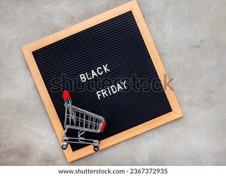 Black Friday written on black notice board with mini shopping cart on mottled grey
