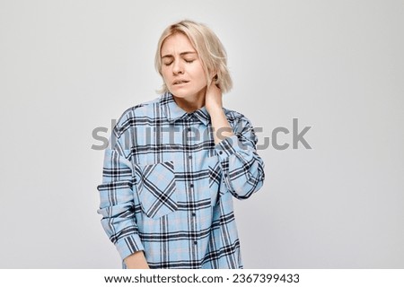 Portrait of young woman suffering from pain, touching neck isolated on white studio background. Psychosomatics of stress, degenerative disease of spine