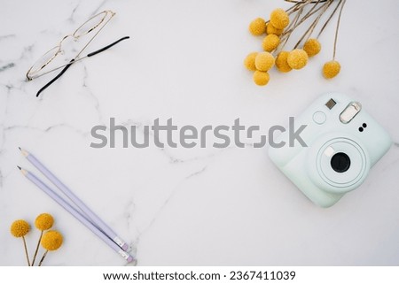 Flat lay of white marble table with stationery, glasses, yellow flowers and photo camera. Top view with copy space. Modern female work place concept