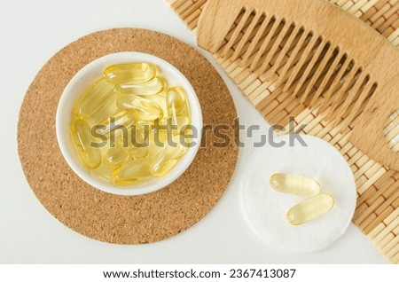 Small white bowl with cosmetic oil (face serum, cod liver oil, vitamin A, D, E) capsules. Natural health care, skin care and hair treatment recipe. Royalty-Free Stock Photo #2367413087