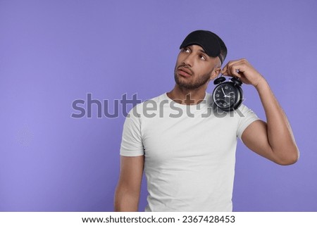 Tired man with alarm clock on violet background, space for text. Insomnia problem