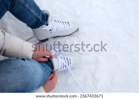 A woman sitting on a bench in the park puts on figure skates and ties her shoelaces with her hands, close-up view