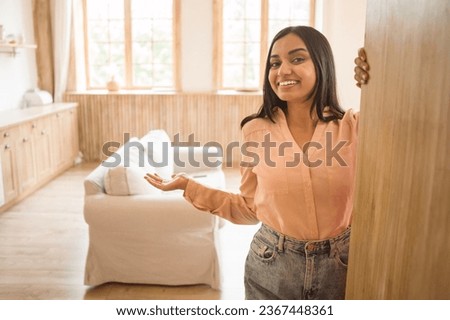 Welcome to my home. Happy indian lady opening door and gesturing inviting to come in, smiling to camera, free space. Real estate owner, hospitality concept Royalty-Free Stock Photo #2367448361