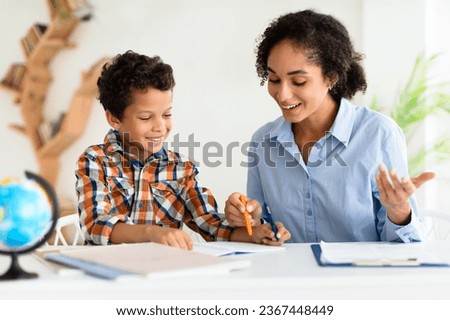 Kid Education And Tutoring. Young School Teacher Lady Teaching Kid Boy, Explaining Lesson To Him Sitting Together At Table Indoors, Writing And Taking Notes. Help In Study, Mentorship
