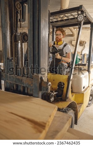 Male craftsman at wooden sawmill warehouse is loading with loader wooden board. High quality photo