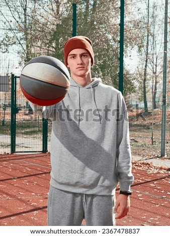 A teenager in a gray tracksuit and a brown cap with a ball in his hands.  Athlete on the basketball court. Basketball player. Sports equipment.