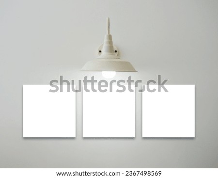 Mockup three square white blank picture frames set hanging under the vintage glowing light lamp on white background, minimal style. Template space for photography or painting decoration on the wall.