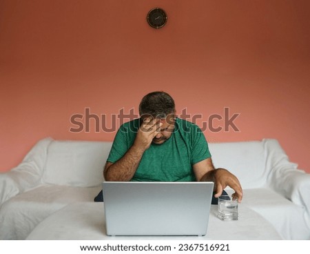 Tired person, sick or stressed businessman holding glass with drinking water at home in living room. working space. man,  with hangover is tormented by thirst. male with headache.                     Royalty-Free Stock Photo #2367516921