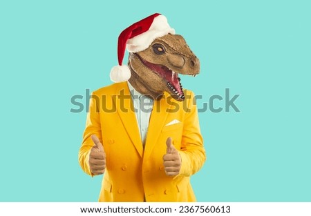 Funny man in dinosaur mask gesturing two thumbs up showing approval sign of your Christmas choice. Man with dinosaur head, in Santa Claus hat and in yellow jacket isolated on turquoise background.