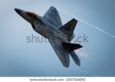 A modern military jet fighter aircraft gliding through an azure sky, producing a white trail of smoke from its engines Royalty-Free Stock Photo #2367566043