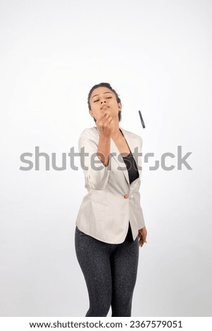 Corporate office lady with black hair having playful moment with pen in formal wear wearing white blazer against white background. 