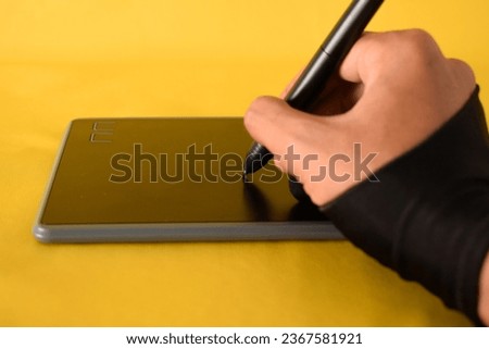 The hand wearing glove draws on a graphics tablet. Freelance, designer, Illustrator on yellow background