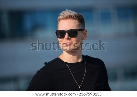 young man in a black T-shirt and black sweatpants and black sunglasses against the background of city buildings