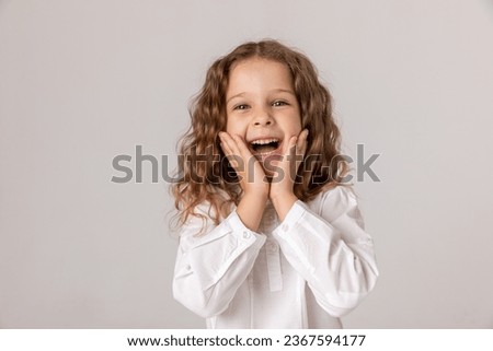 Cheerful girl about 5-6 years old in white shirt holding her hands near her face and happy smile on white background. happy child enjoys success and victory. Discounts and sales. Advertising concept Royalty-Free Stock Photo #2367594177