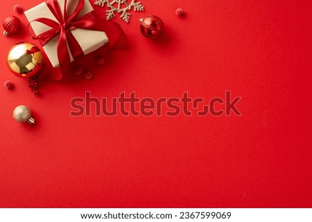 Cheers to the New Year! Overhead view of craft gift box, holiday ornaments, baubles, snowflake, scattered mistletoe berries against a red backdrop, offering room for your holiday wishes or promotion Royalty-Free Stock Photo #2367599069