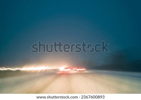 Driving in bad weather conditions with snow on night highway,  motion blur with light trails created by long exposure photography