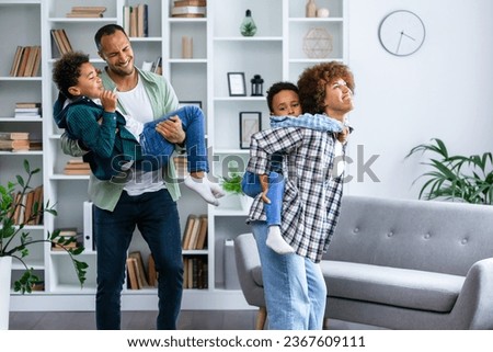 Happy parents with kids dancing in modern living room, having fun, playing active game, overjoyed mother and father with children siblings dancing to favorite music, jumping, celebrating event
