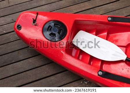Red plastic kayak and white paddle lay on a wooden flooring, top view Royalty-Free Stock Photo #2367619191