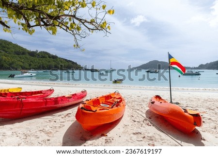 Beach landscape with red plastic kayaks and Seychelles flag on a sunny day Royalty-Free Stock Photo #2367619197