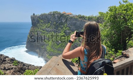 Young woman taking photos of Pura Luhur Uluwatu temple, young woman traveling around Bali island Royalty-Free Stock Photo #2367625993