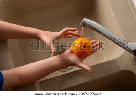 children's hands washing an orange in the kitchen
