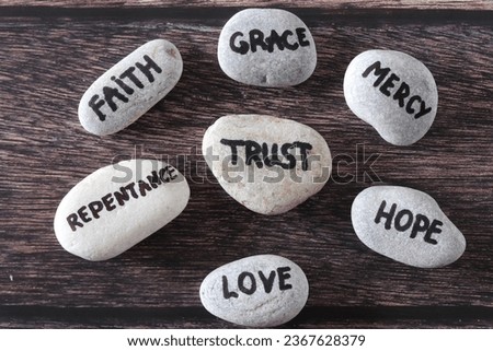 Trust, mercy, faith, grace, love, repentance, and hope handwritten words on stones. Top view. Christian foundation and obedience to God Jesus Christ, biblical concept.