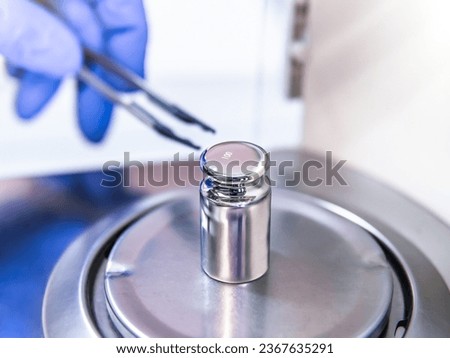 A operator's hand is holding steel calibration weight to place on the analytical balance. Concept of quality control in a laboratory. Royalty-Free Stock Photo #2367635291