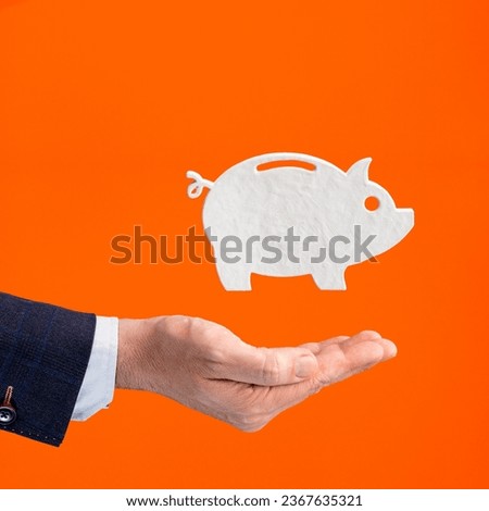 Businessman hand holding piggy bank icon - Savings concept on orange background
