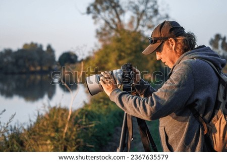 Photographer is setting up camera on tripod outdoors. Man photographing landscape or wildlife at lake