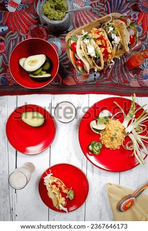 A variety of tacos on plates on wooden table with table cloth design
