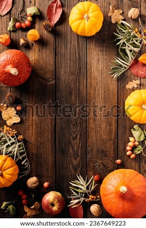 Frame of pumpkins, autumn leaves, berries, pine cones, sea ​​​​buckthorn on wooden table. Happy Thanksgiving day vertical banner template
