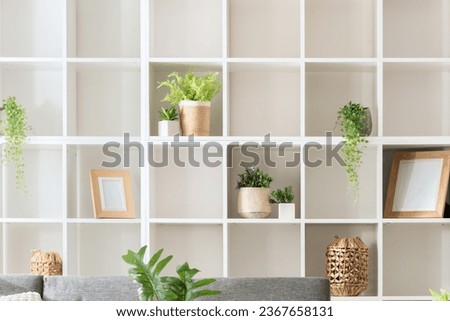 Modern Minimalist Living Room Interior Design Featuring a White Square-Spaced Bookshelf, Grey Sofa, and Plants, Neatly Organized for a Homey Ambience, Illuminated by Natural Light. Royalty-Free Stock Photo #2367658131