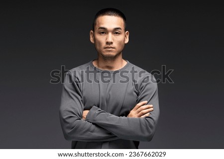 Serious, emotionless young Asian man standing isolated on black background, looking at camera. Attractive male wearing casual clothes, advertisement concept