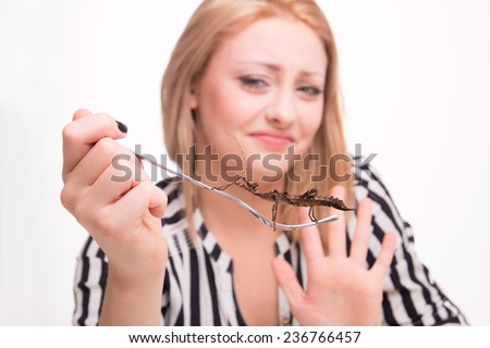 Disgusted woman eating big insects with a fork in a restaurant 
