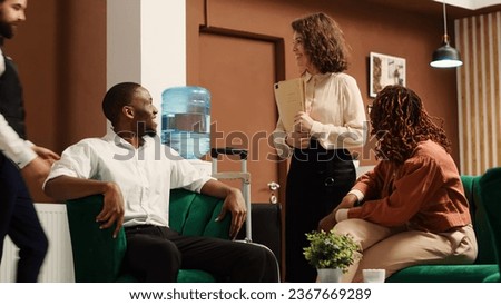 Positive friendly hotel manager greeting in tourists on vacation trip while they wait to be checked in their rooms. Relaxed guests happy with customer service provided by helpful concierge personnel Royalty-Free Stock Photo #2367669289
