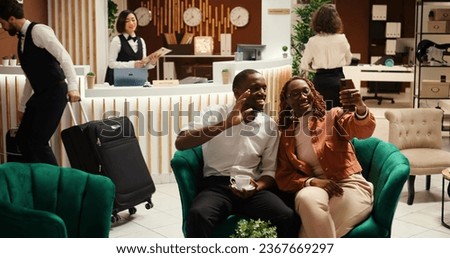 Happy husband and wife in video conference with mates during hotel stay. Relaxed couple on their honeymoon trip in video call with friends while enjoying cup of coffee in resort lobby Royalty-Free Stock Photo #2367669297