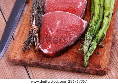 prime fillet meat : dry raw beef on cutting board with asparagus , thyme bundle , color peppercorn mix and red paprika powder mixed with dry spices over wooden table ready to cooking