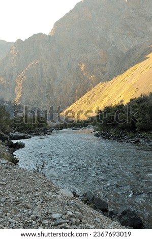 A small stormy river in the rays of the mountains of the setting sun flows along the bottom of a deep canyon on a warm autumn evening. Chulyshman river, Altai, Siberia, Russia.
