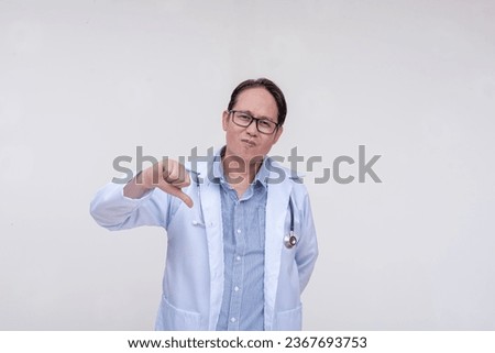 An unimpressed and dismissive doctor gives the thumbs down sign. Of asian descent, middle aged male in his 40s. Isolated on a white background. Royalty-Free Stock Photo #2367693753