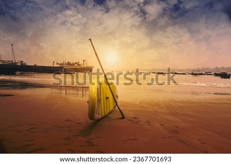 tihs picture captures the peacefulness of a summer sunset on the beach, with the silhouette of a paddle boarder on the shoreline.