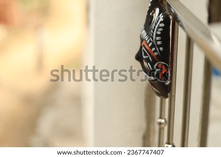 A black Indian devil mask or raksha kawach tied to the house balcony outside from side angle