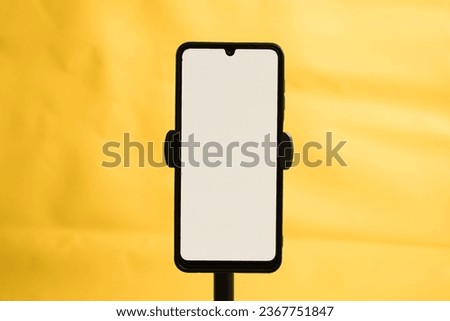 Portrait phone with white screen fixed to tripod on yellow background, for mockup design.
