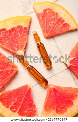 Ampoules with vitamin C and grapefruit slices on white tile background